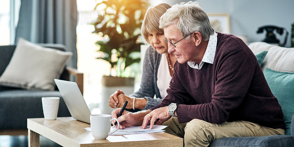 older couple filling out paperwork on a coffee table in front of a laptop