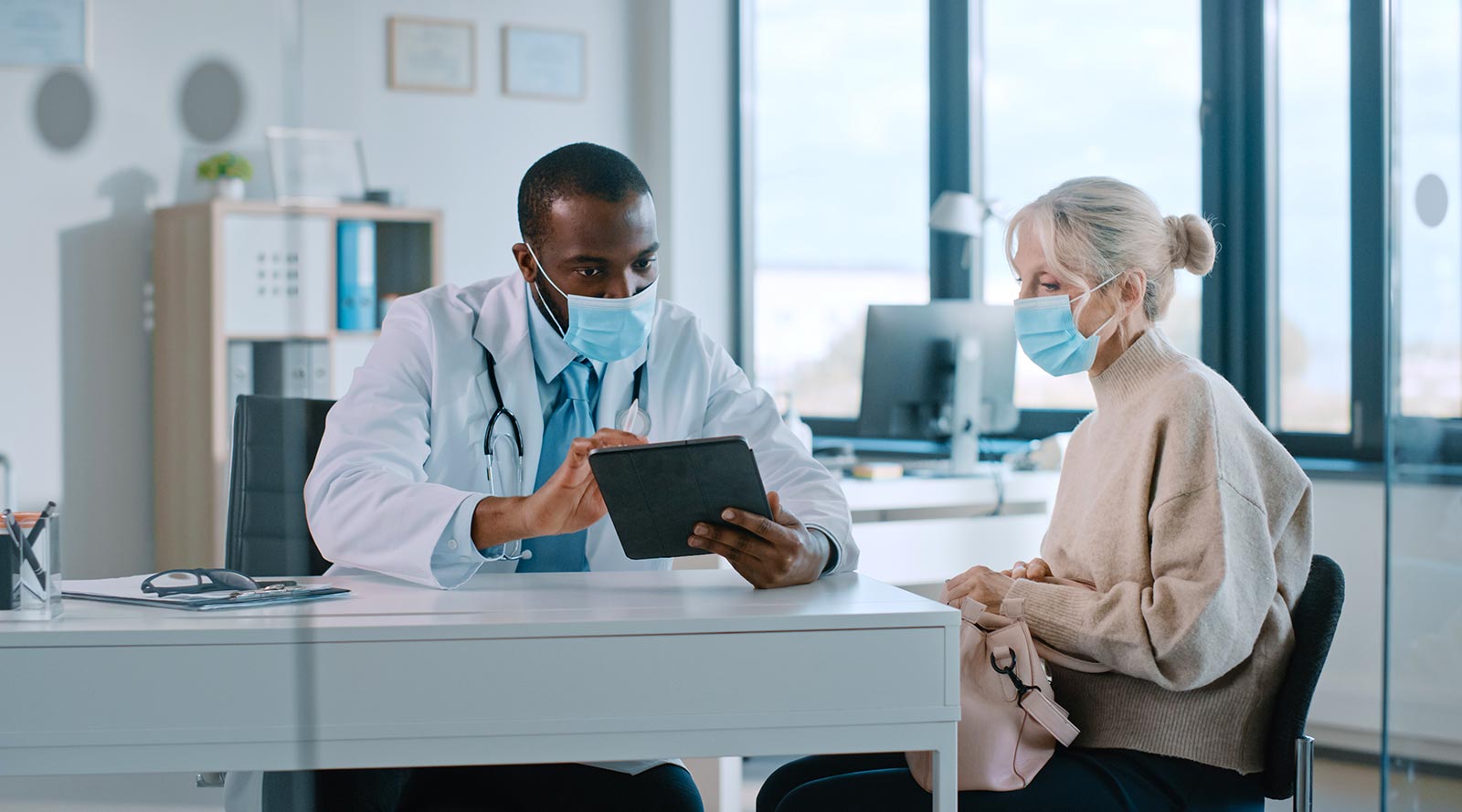 Doctor and patient looking at tablet wearing masks