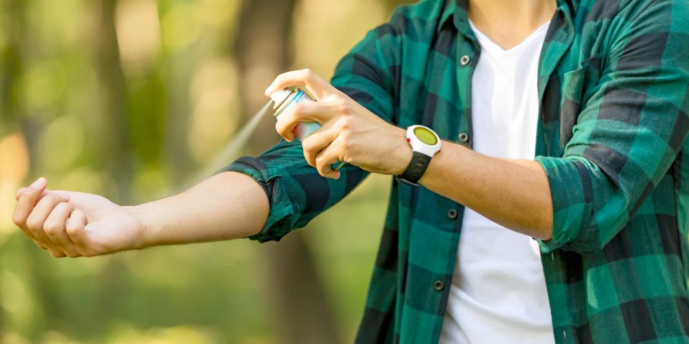 A young man sprays insect repellent on his arm.