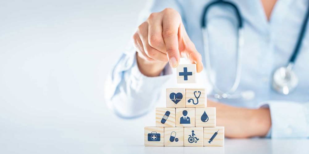 Person wearing stethoscope stacking wooden blocks with healthcare related icons on them