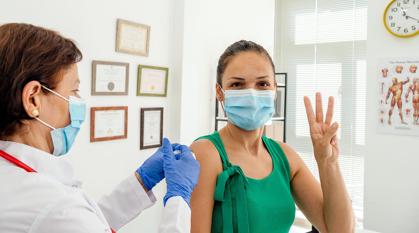 woman holding up three fingers while receiving a vaccination