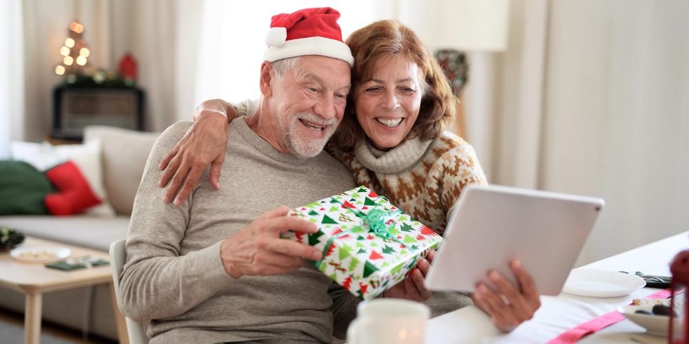 Couple holding a gift talking to someone through a tablet video call.